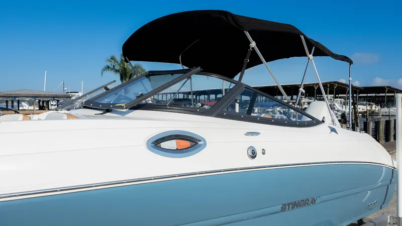 Slide: The Image of 2025 Stingray 231DC boat with black canopy docked at marina. - 32