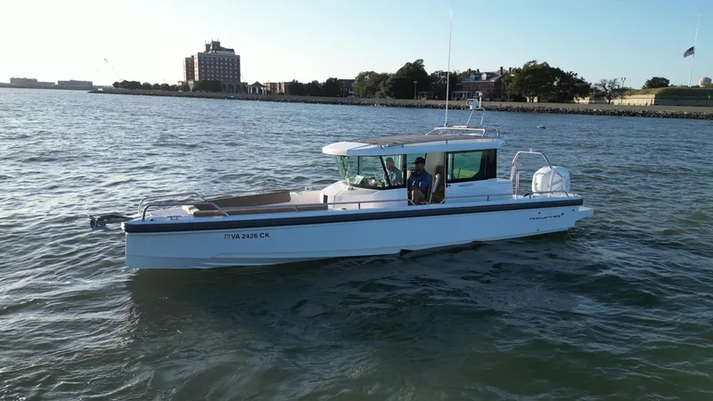 Slide: The Image of 2019 Axopar 28 CABIN boat cruising on a calm waterway near a city shoreline. - 1