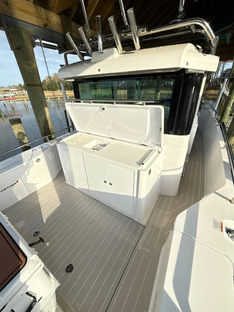 Slide: The Image of 2019 Axopar 28 CABIN boat with open storage compartment, docked under a wooden structure. - 25