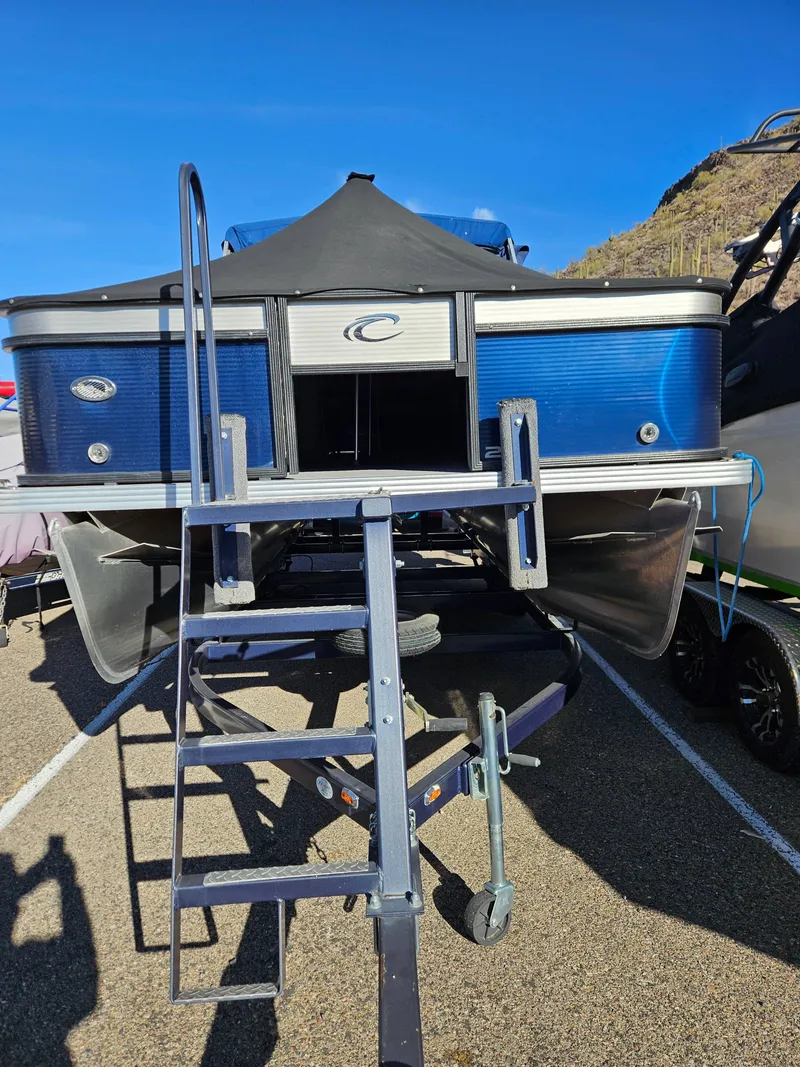 Slide: The Image of 2018 Crest 200 CA pontoon boat with ladder, parked on a trailer under clear blue sky. - 3