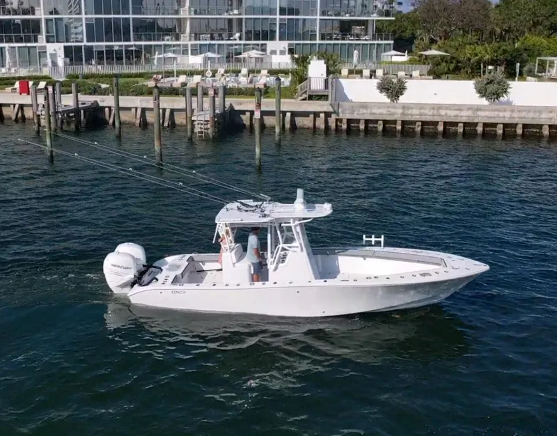 Slide: The Image of 2018 Conch 30 boat cruising near a modern waterfront building. - 23