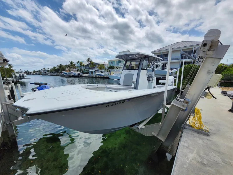 Slide: The Image of 2022 Costa Custom Boats 264 HC on lift by waterfront homes under cloudy sky. - 1