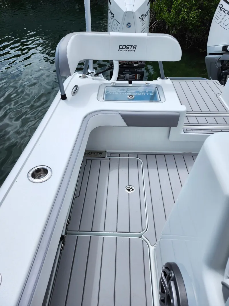 Slide: The Image of 2022 Costa Custom Boats 264 HC deck with seating and storage, near water. - 12