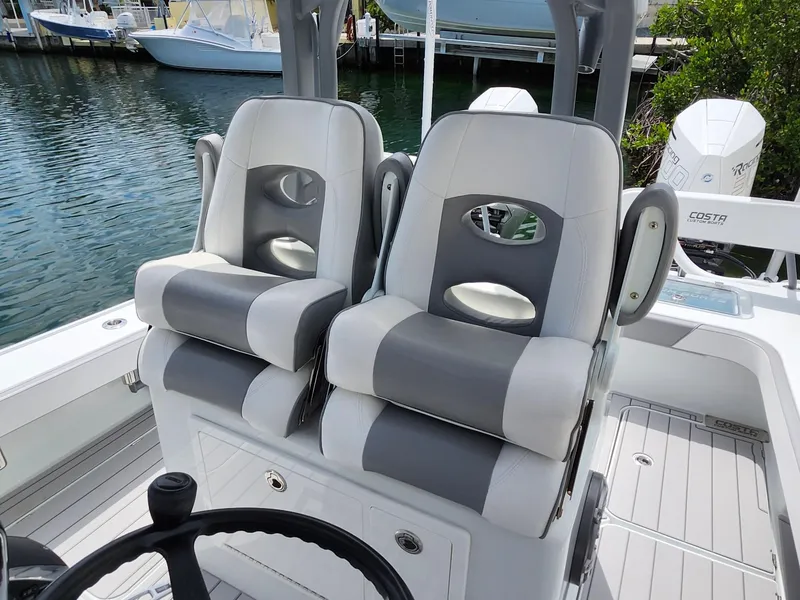 Slide: The Image of 2022 Costa Custom Boats 264 HC helm seats, gray and white, on a sleek deck by the water. - 19