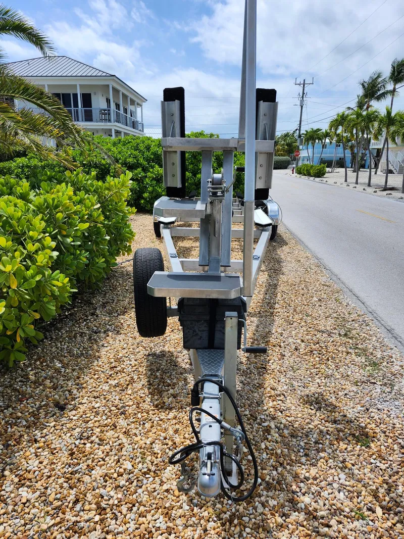 Slide: The Image of Boat trailer for 2022 Costa Custom Boats 264 HC on gravel path, surrounded by greenery. - 28