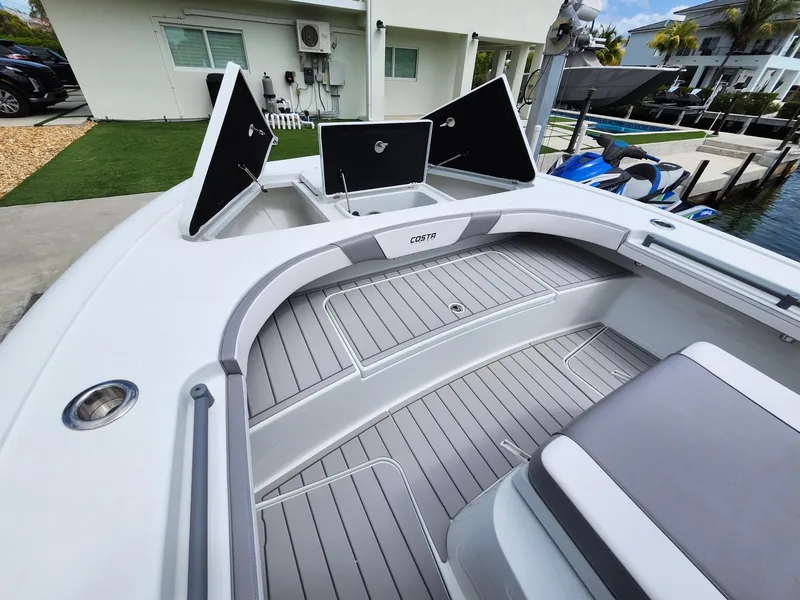 Slide: The Image of 2022 Costa Custom Boats 264 HC deck with open storage compartments, docked near modern homes. - 6
