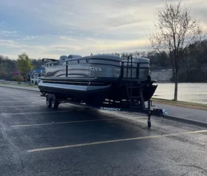 Slide: The Image of 2024 Regency 250 LE3 pontoon boat on trailer, parked by a scenic lake. - 4