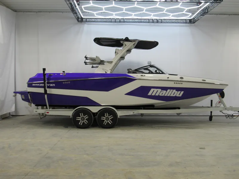 The Image of 2025 Malibu Wakesetter 24 MXZ boat in a showroom, featuring a sleek purple and white design. - 0