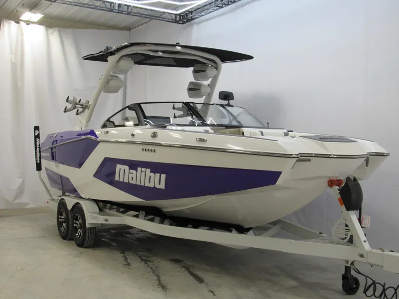 Slide: The Image of 2025 Malibu Wakesetter 24 MXZ boat in a showroom, featuring a sleek purple and white design. - 2
