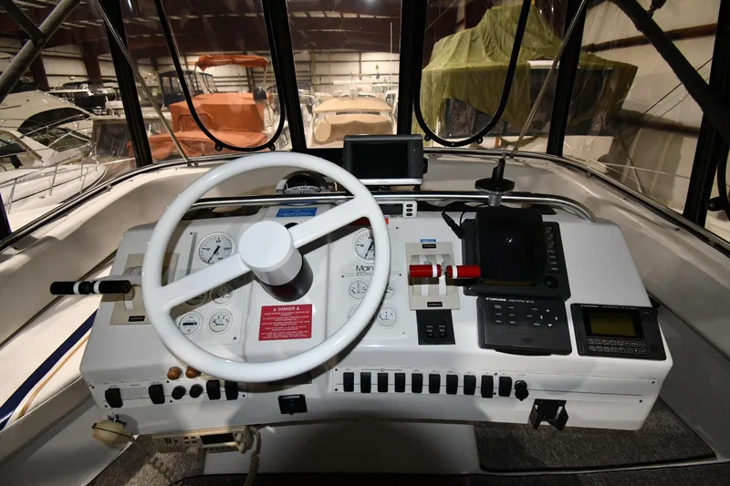 Slide: The Image of 1997 Mainship 40 Sedan Bridge helm with steering wheel and control panel in a marina setting. - 16