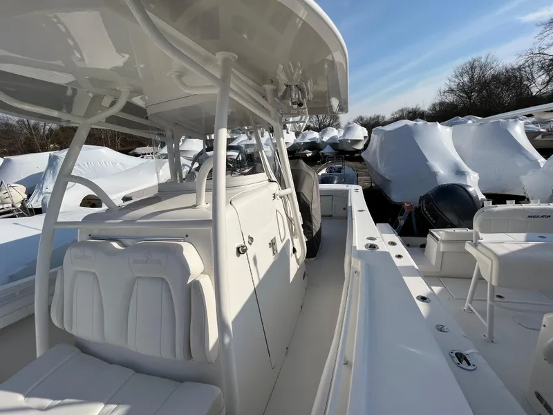 Slide: The Image of 2018 Regulator 31 boat interior with white seating and console, docked among covered boats. - 18