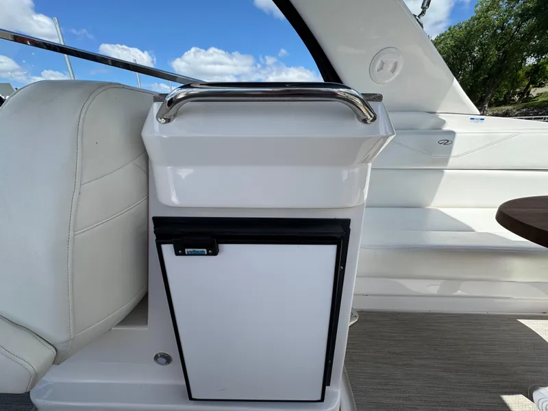 Slide: The Image of 2011 Regal 3350 Cuddy interior with white seating and compact fridge under blue sky. - 28