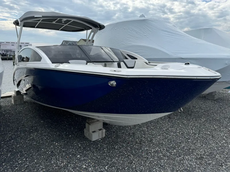 Slide: The Image of 2021 Yamaha Boats 275SE, blue and white, docked on gravel under cloudy sky. - 2