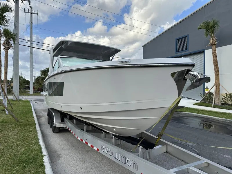 Slide: The Image of 2020 Aviara AV32 OB boat on trailer, parked outdoors near palm trees and industrial building. - 3