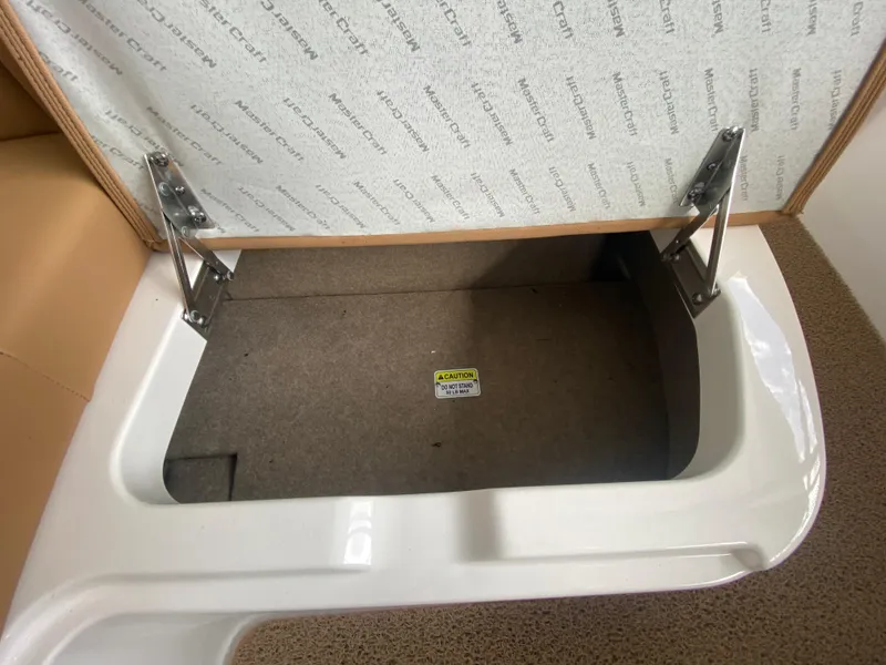 Slide: The Image of Open storage compartment in 2020 MasterCraft X26 boat with visible hinges and carpeted interior. - 41
