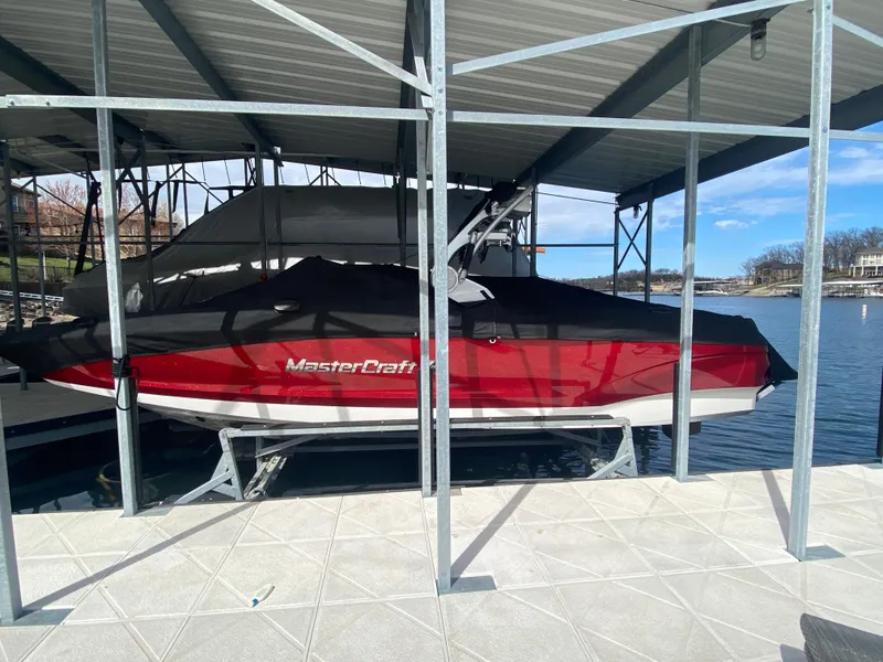 Slide: The Image of 2020 MasterCraft X26 boat docked under a metal canopy on a sunny day. - 48