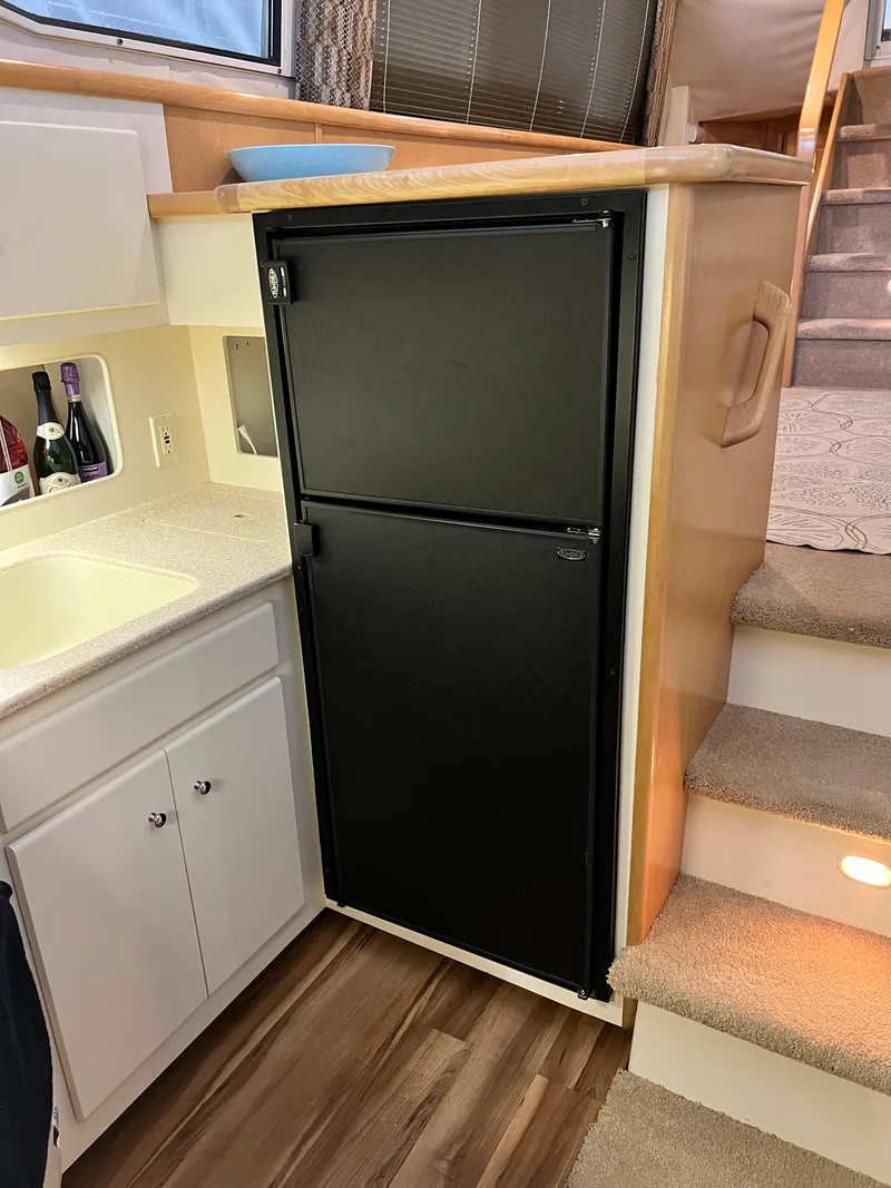 Slide: The Image of 1998 Carver 405 Aft Cabin interior with black fridge, white cabinets, and carpeted stairs. - 11