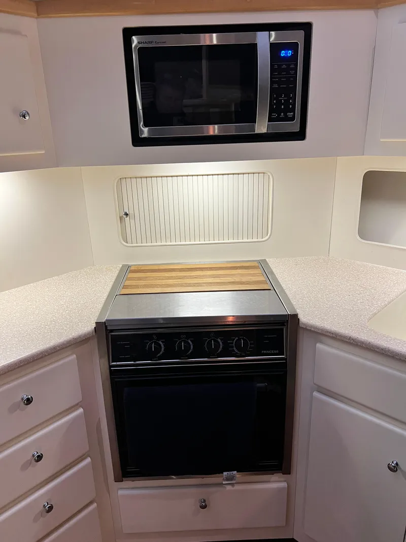 Slide: The Image of 1998 Carver 405 Aft Cabin kitchen with microwave and stove, featuring white cabinetry. - 12
