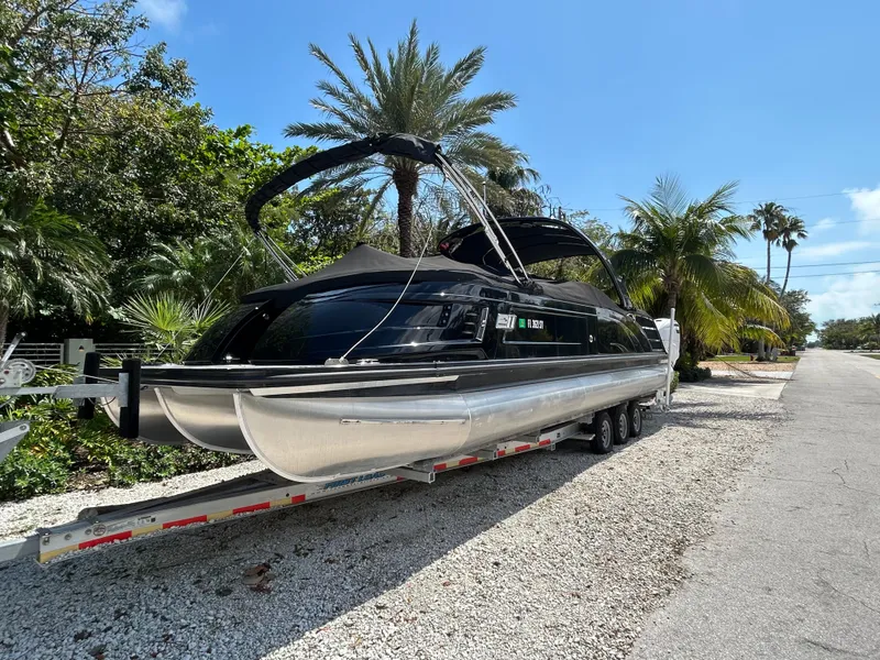 Slide: The Image of 2021 Bennington 30 pontoon boat on trailer, surrounded by tropical trees. - 1