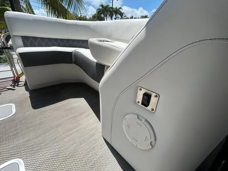 Slide: The Image of 2021 Bennington 30 boat interior with white and gray seating, textured flooring, and palm trees in background. - 14