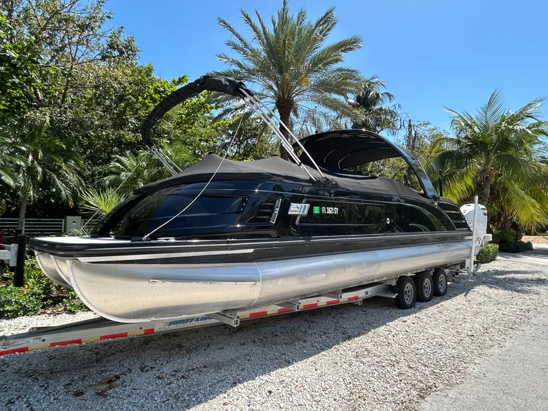 Slide: The Image of 2021 Bennington 30 pontoon boat on trailer, surrounded by palm trees. - 2