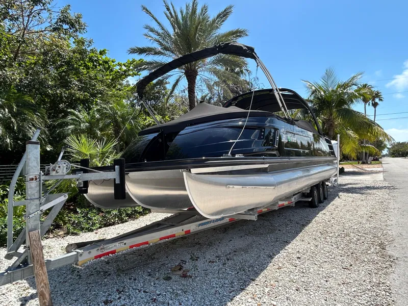 Slide: The Image of 2021 Bennington 30 pontoon boat on trailer, surrounded by tropical trees. - 3