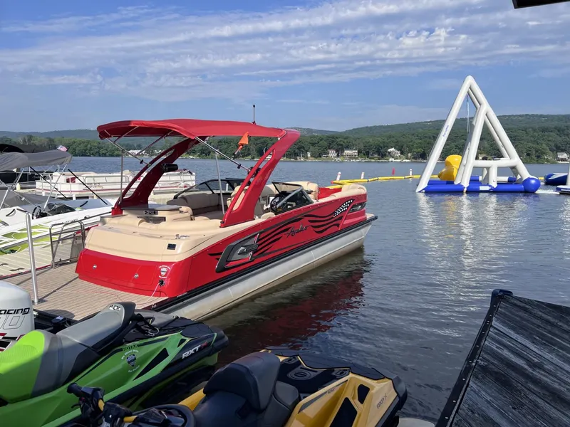 Slide: The Image of Red 2022 Avalon Excalibur Elite Windshield boat docked near inflatable water park. - 1