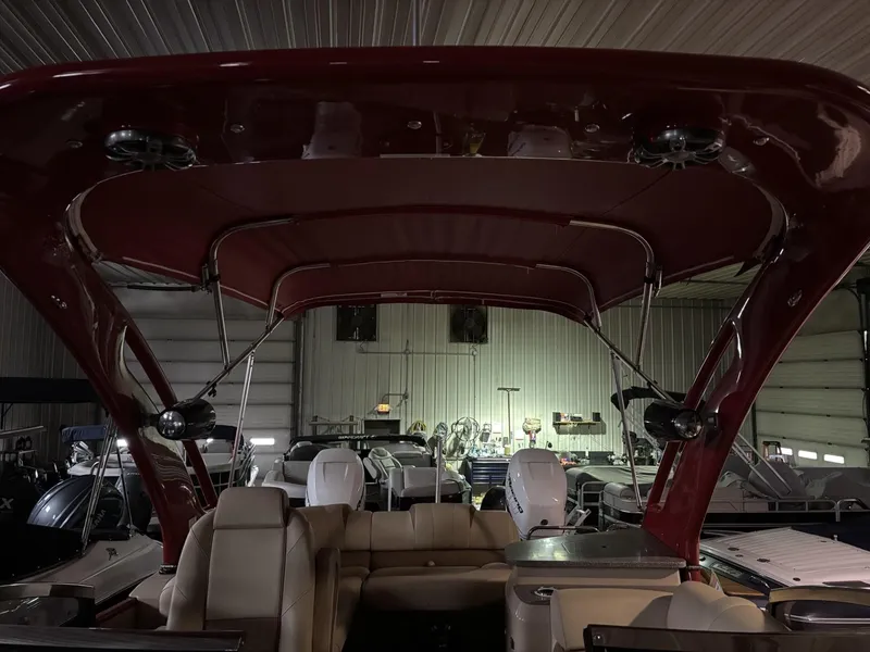 Slide: The Image of 2022 Avalon Excalibur Elite Windshield boat interior with red canopy in a storage facility. - 19