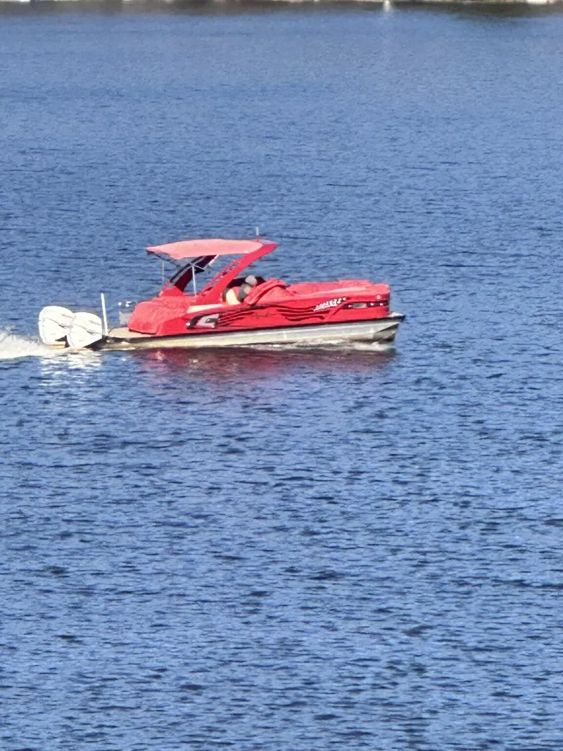 Slide: The Image of Red 2022 Avalon Excalibur Elite Windshield boat cruising on a calm lake. - 3
