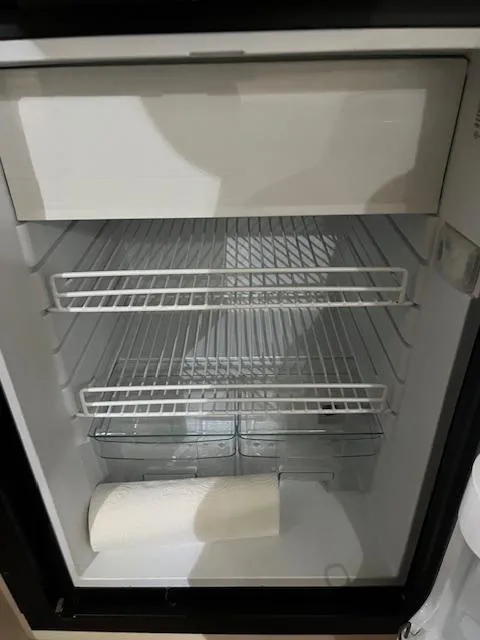Slide: The Image of Empty refrigerator inside a 1996 Sea Ray 330 Sundancer boat, featuring wire shelves and a paper towel roll. - 32