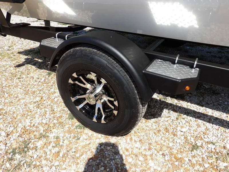 Slide: The Image of 2025 Crestliner XFC 189 trailer wheel on gravel, featuring sleek black and silver alloy design. - 35