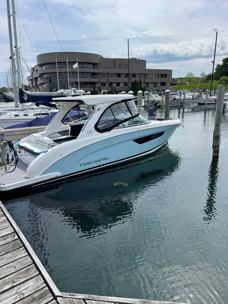 Slide: The Image of 2023 Regal 3300 boat docked in a marina with modern building in background. - 0