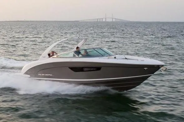 Slide: The Image of 2023 Regal 3300 Bowrider cruising on open water with distant bridge view. - 24