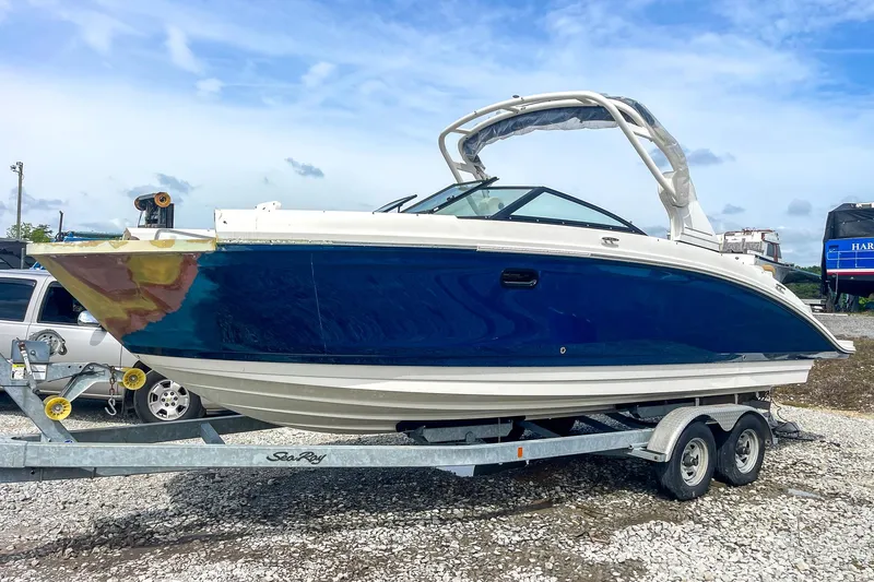 Slide: The Image of 2019 Sea Ray 270 Sundeck SDX boat on trailer, blue hull, parked outdoors. - 2