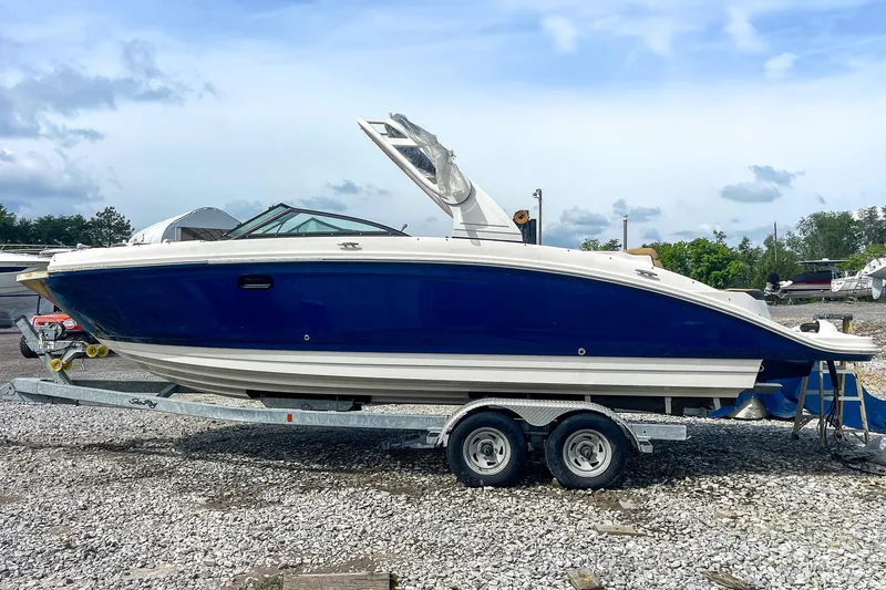 Slide: The Image of 2019 Sea Ray 270 Sundeck SDX boat on trailer, blue hull, parked on gravel. - 3