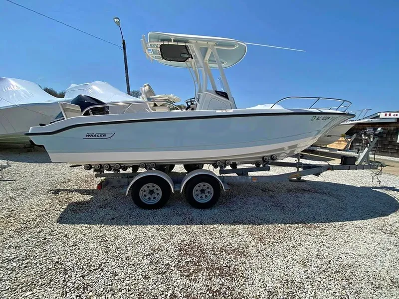 Slide: The Image of 2023 Boston Whaler 220 Dauntless boat on a trailer, parked on gravel. - 0
