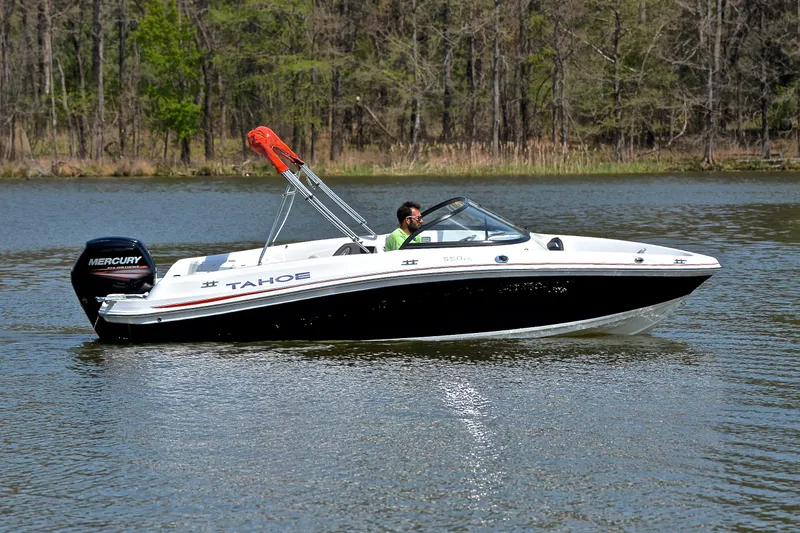 Slide: The Image of 2018 Tahoe 550 TS boat cruising on a calm lake with wooded shoreline. - 7