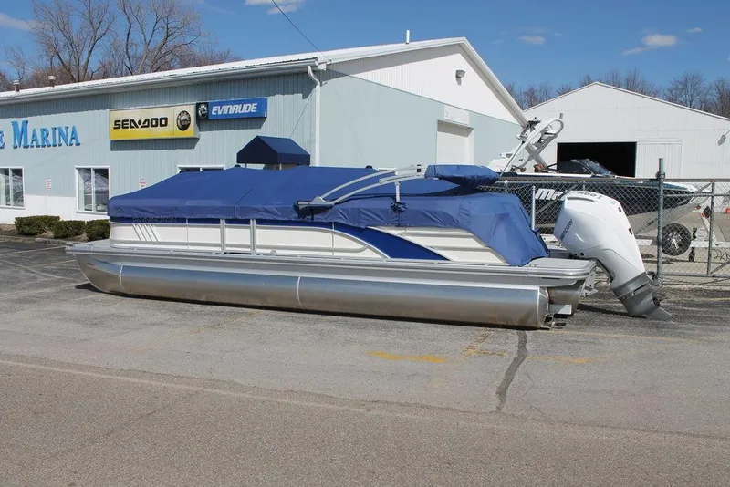 Slide: The Image of 2025 Bennington L Quad Bench 25 LFB pontoon boat with blue cover, parked outside a marina. - 14