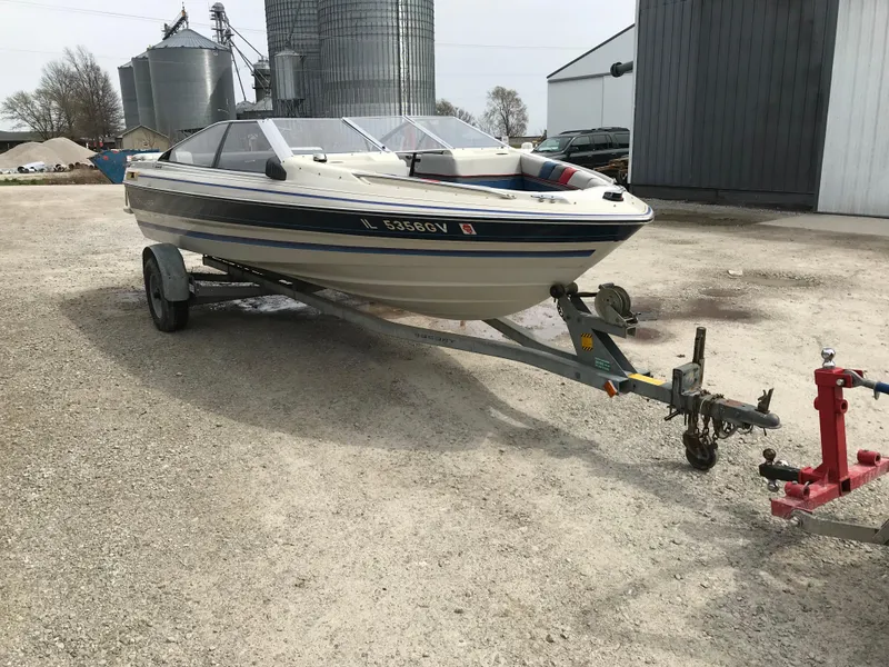 Slide: The Image of 1987 Bayliner 1950 Capri boat on trailer, parked outdoors near industrial buildings. - 2