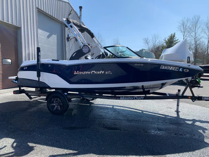 Slide: The Image of 2023 MasterCraft NXT20 boat on trailer, parked outdoors near a building. - 1