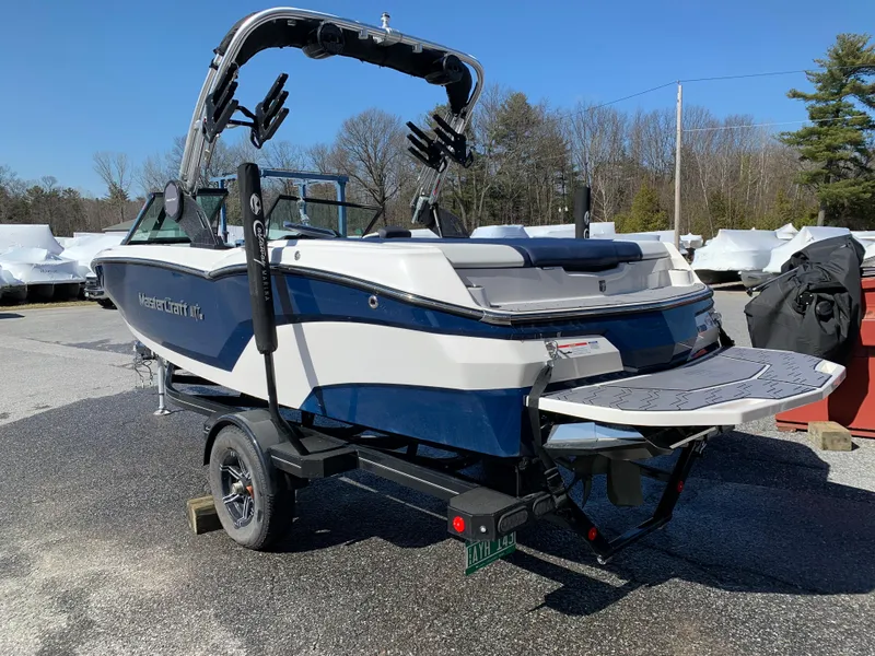 Slide: The Image of 2023 MasterCraft NXT20 boat on trailer, blue and white design, parked outdoors. - 6