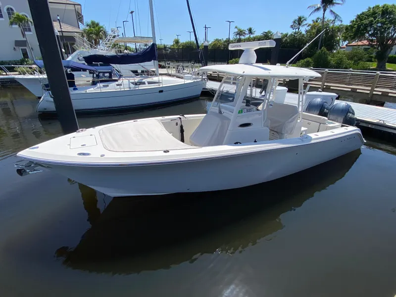 Slide: The Image of 2022 Cobia 301 Center Console boat docked in a marina, surrounded by sailboats. - 0