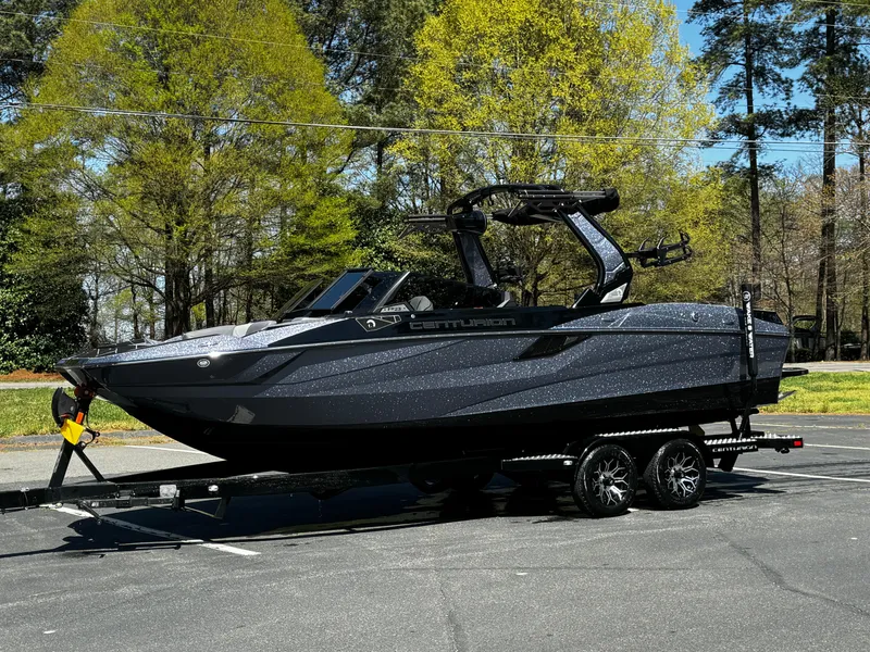 Slide: The Image of 2025 Centurion Fe23 boat on trailer, parked outdoors with trees in background. - 19