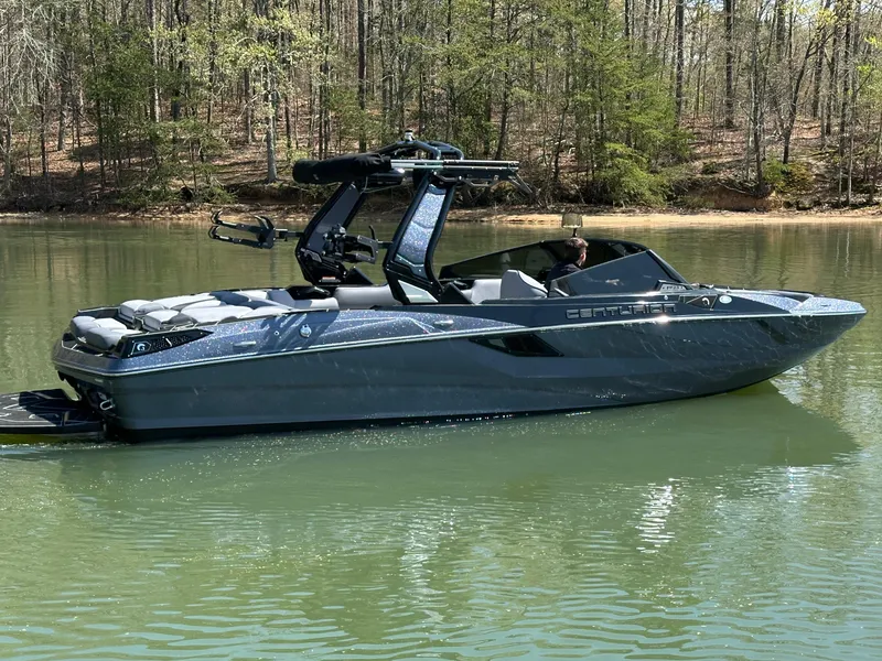 Slide: The Image of 2025 Centurion Fe23 boat on a calm lake surrounded by trees. - 2