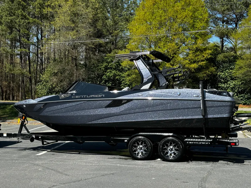 Slide: The Image of 2025 Centurion Fe23 boat on trailer, parked outdoors with trees in the background. - 20