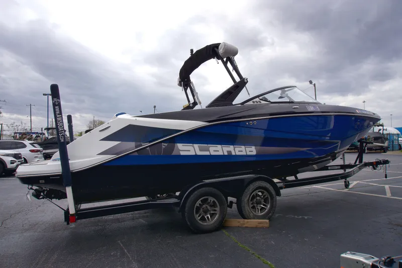Slide: The Image of 2020 Scarab 255 ID boat on trailer, blue and black design, parked outdoors. - 5