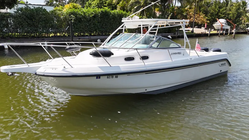 Slide: The Image of 1999 Boston Whaler 28 Conquest boat on calm water, surrounded by lush greenery. - 18