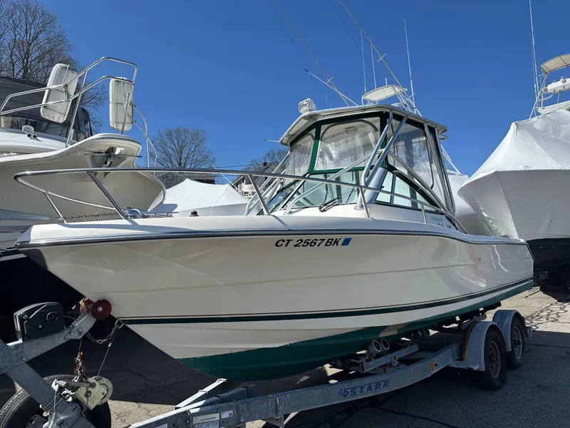 Slide: The Image of 1998 Pursuit 2460 Denali boat on trailer, parked outdoors under clear blue sky. - 0