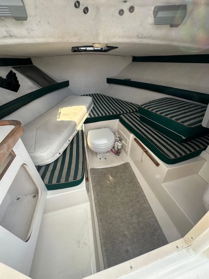 Slide: The Image of 1998 Pursuit 2460 Denali cabin interior with striped cushions and compact toilet. - 11
