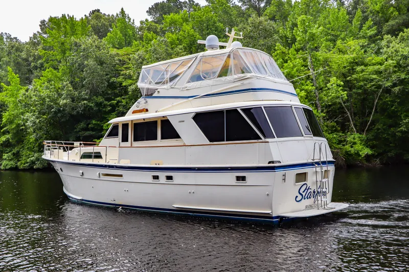 Slide: The Image of 1984 Hatteras 53 Motoryacht cruising on a serene river, surrounded by lush greenery. - 2